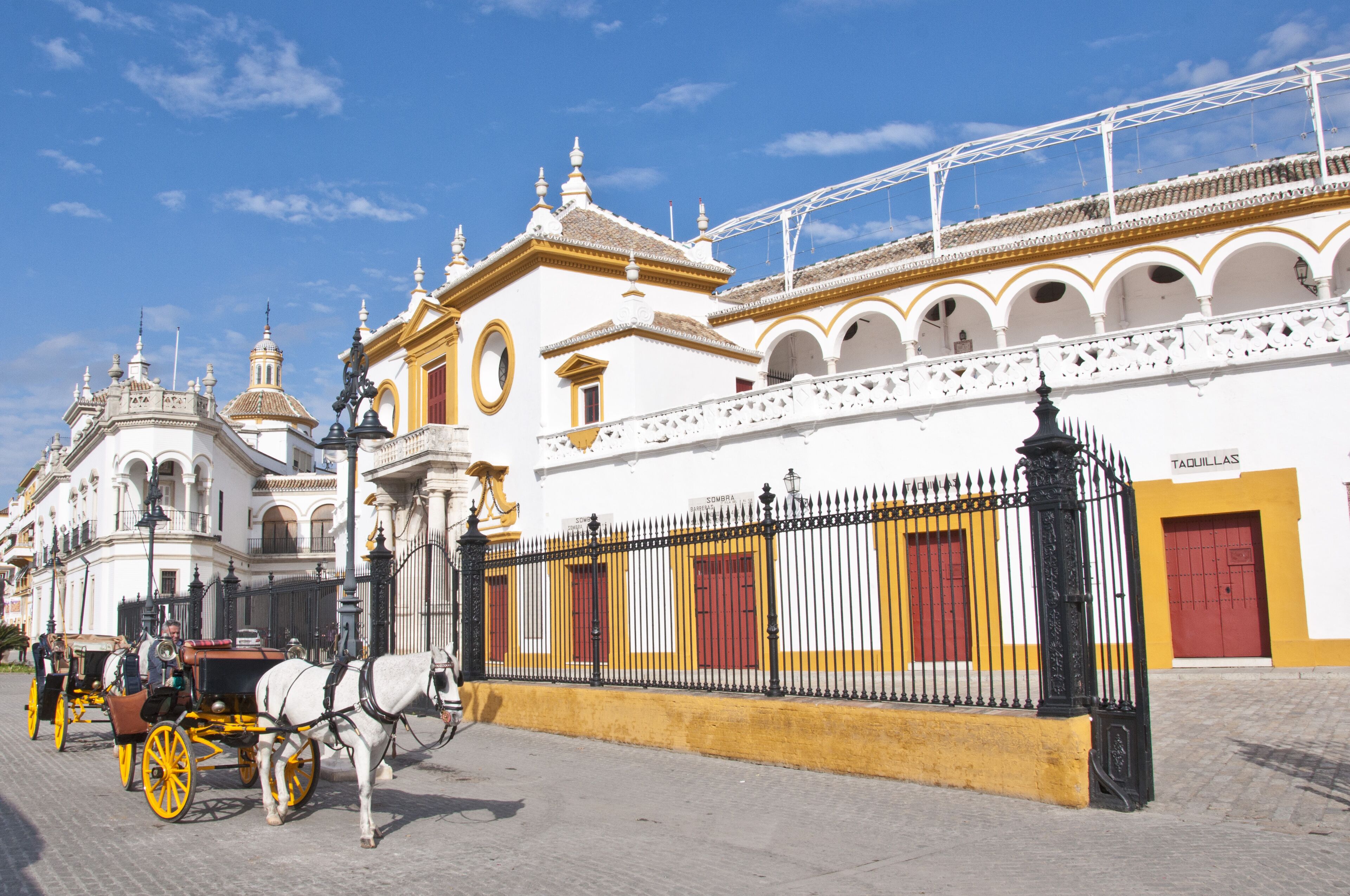 Un edificio histórico con fachada blanca y detalles amarillos, que presenta una entrada destacada con una reja de hierro negra.
