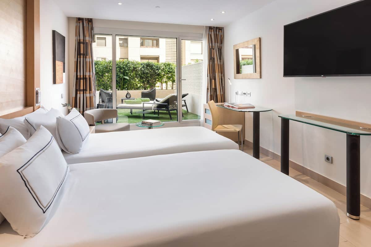 A hotel room with two beds, a TV, a desk, and a balcony with outdoor seating.