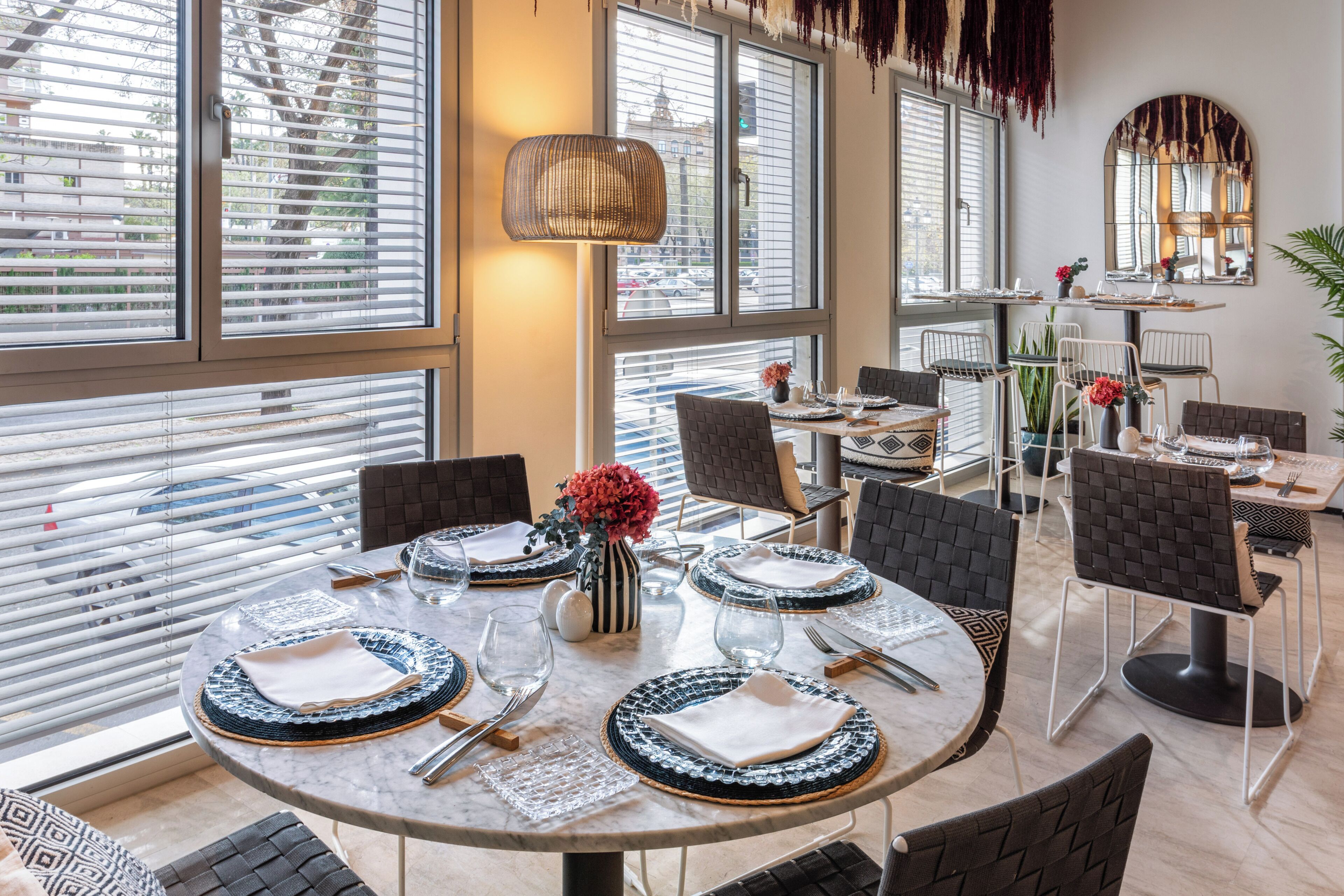 A dining area with round tables, chairs, and a large window with blinds.