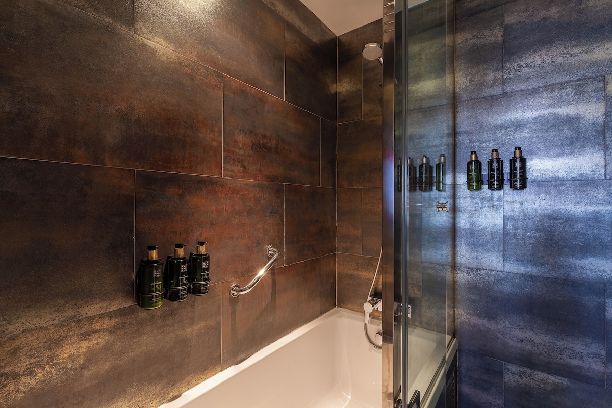 A modern bathroom with a glass shower enclosure, a bathtub, and a wall-mounted handrail.