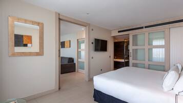 A hotel room with a large bed, a TV mounted on the wall, a glass table, and a seating area with a couch.
