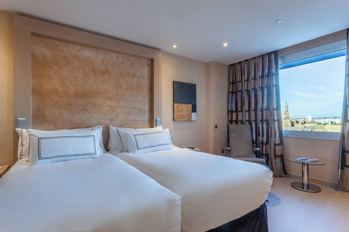 A hotel room with a large bed, a small table, and a view of a distant building.