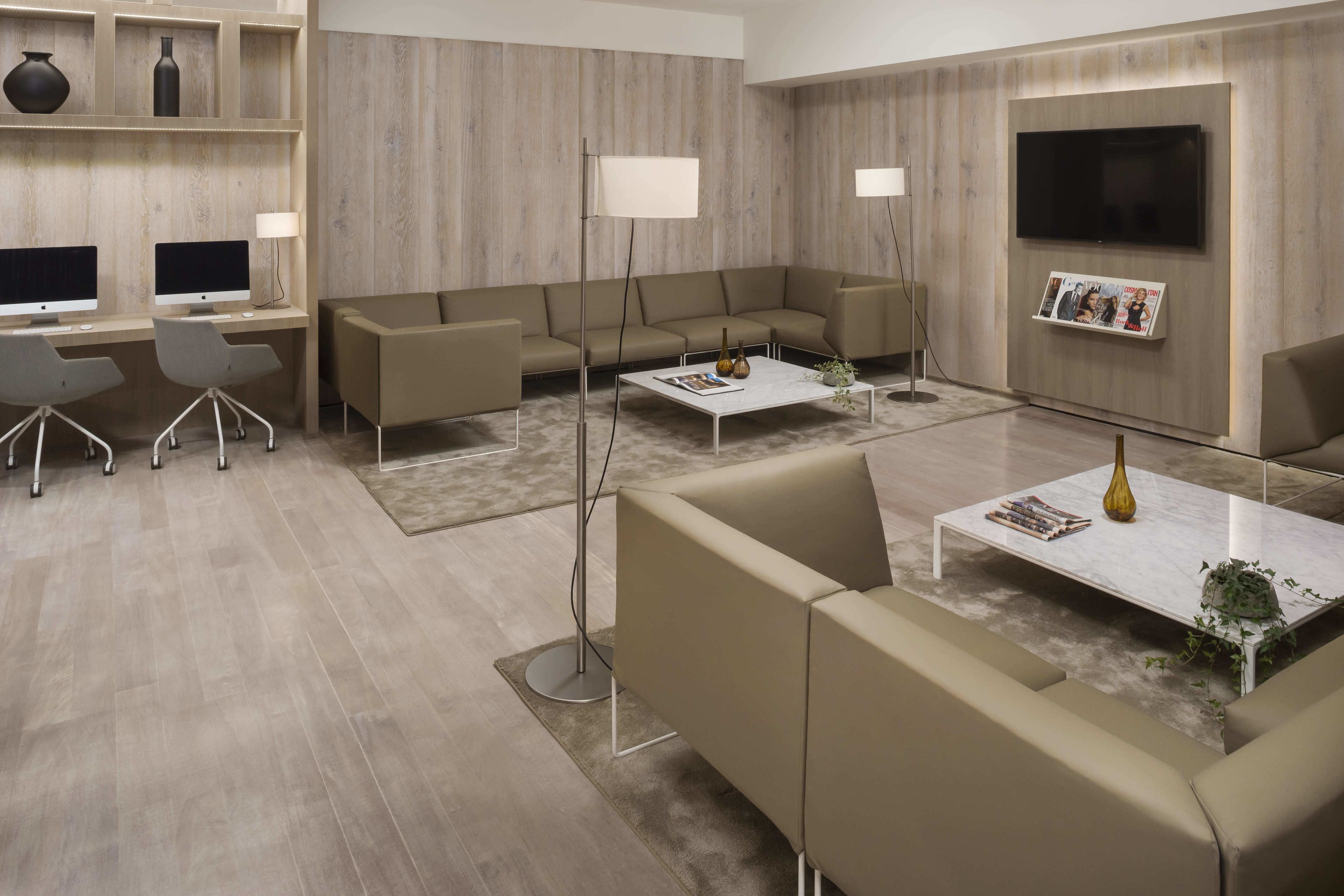 Una sala de estar moderna con un sofá modular, una mesa de centro, un televisor montado en la pared y un escritorio con dos monitores.