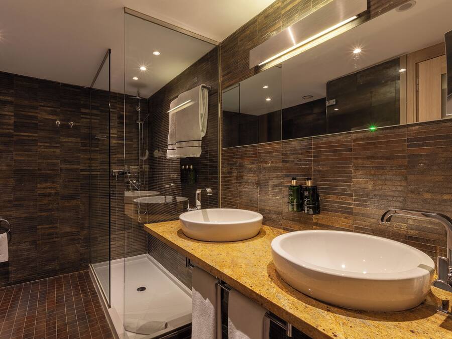 Un baño moderno con dos lavamanos, una ducha con mampara de vidrio y un espejo grande.