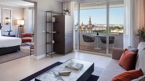 A modern hotel room with a large bed, a glass coffee table, a sofa, a balcony with a city view, and a seating area with a table and chairs. - Melia Sevilla (Seville)