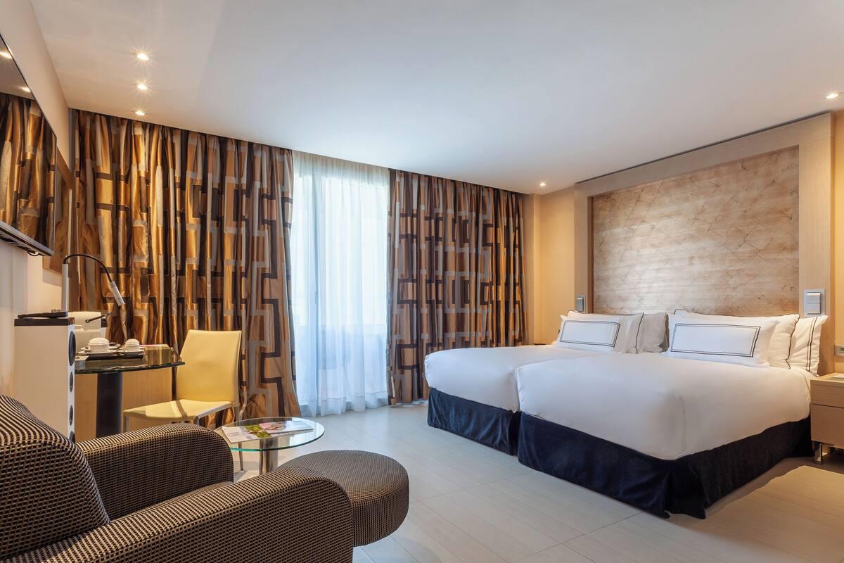 A modern hotel room with a large bed, a desk with a chair, a sofa, and a small round table.