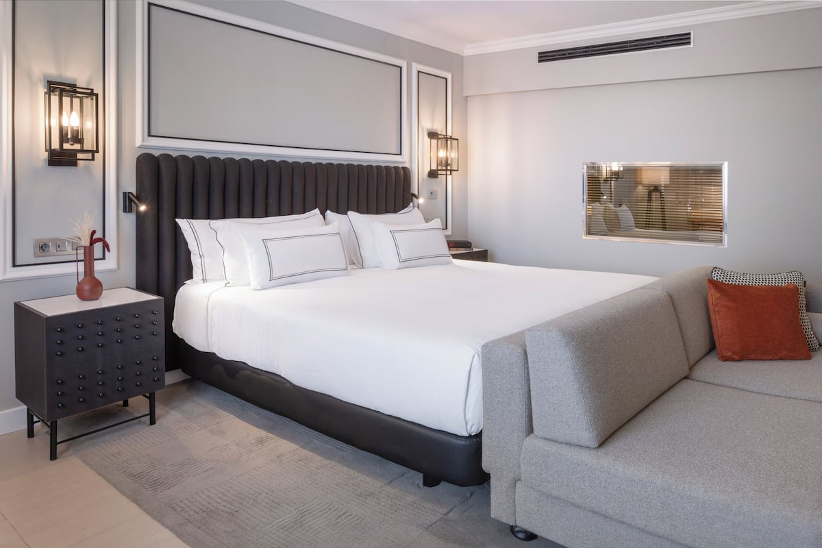 A modern bedroom with a large bed, a nightstand, a dresser, and a sofa.