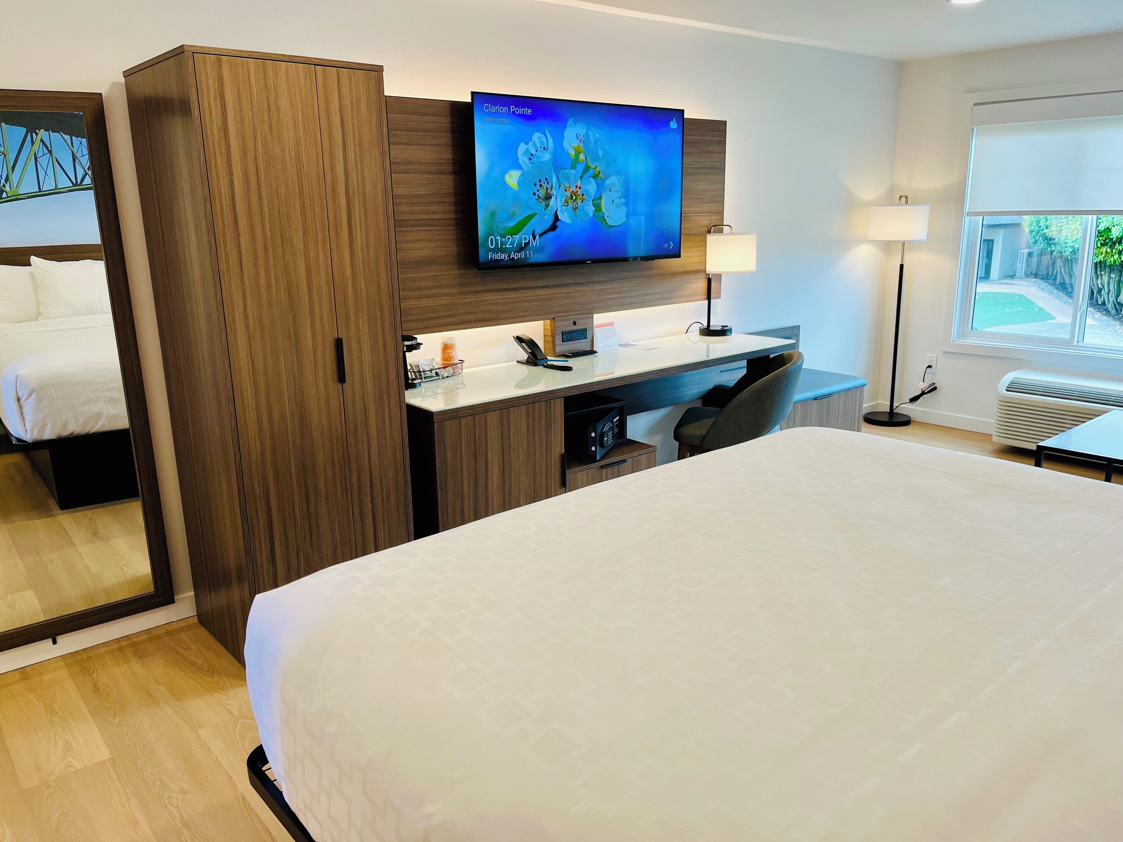 A hotel room with a large bed, a desk with a computer, a TV, and a window with a view.