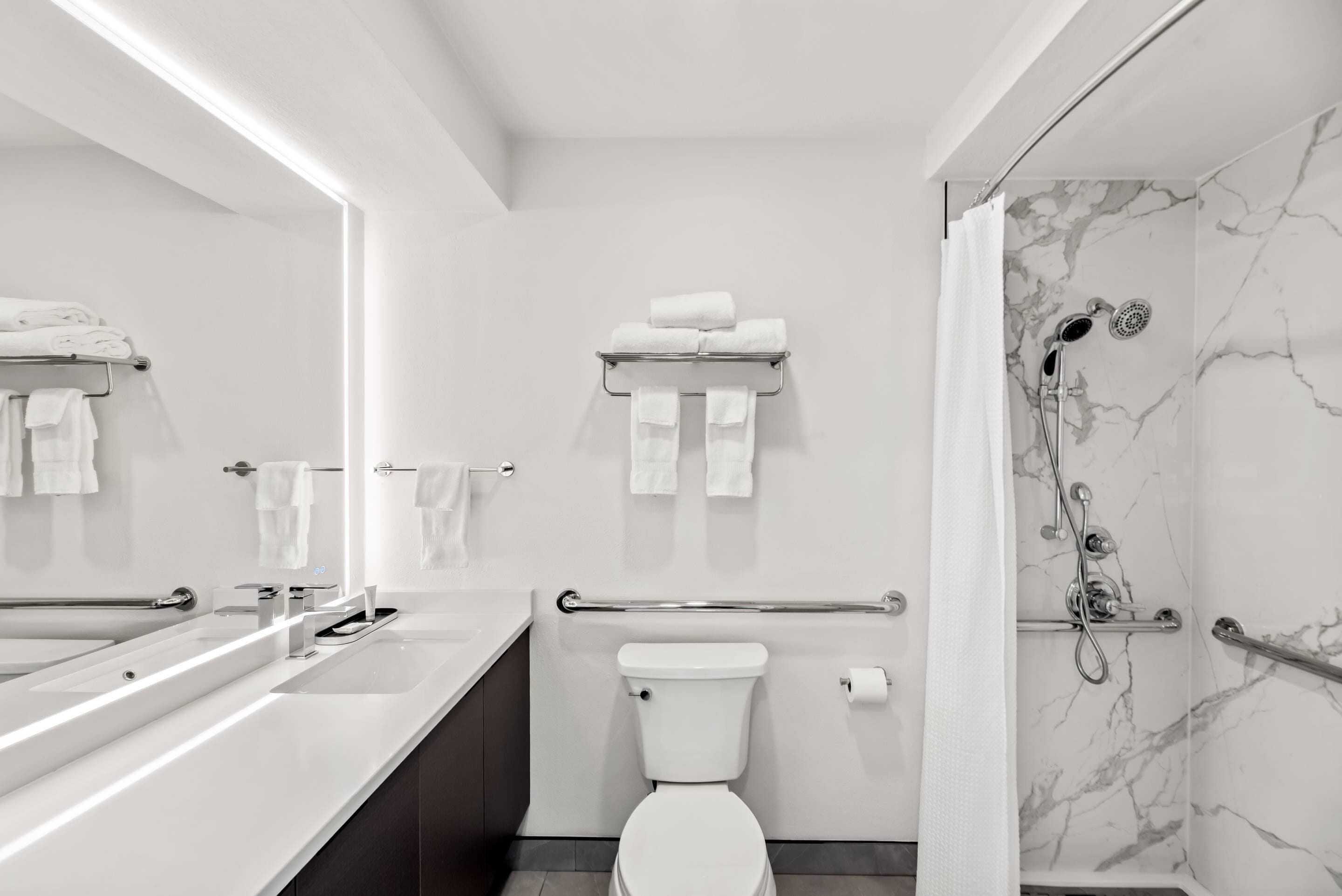 A modern bathroom with a large mirror, white fixtures, a toilet, and a shower area with marble walls.