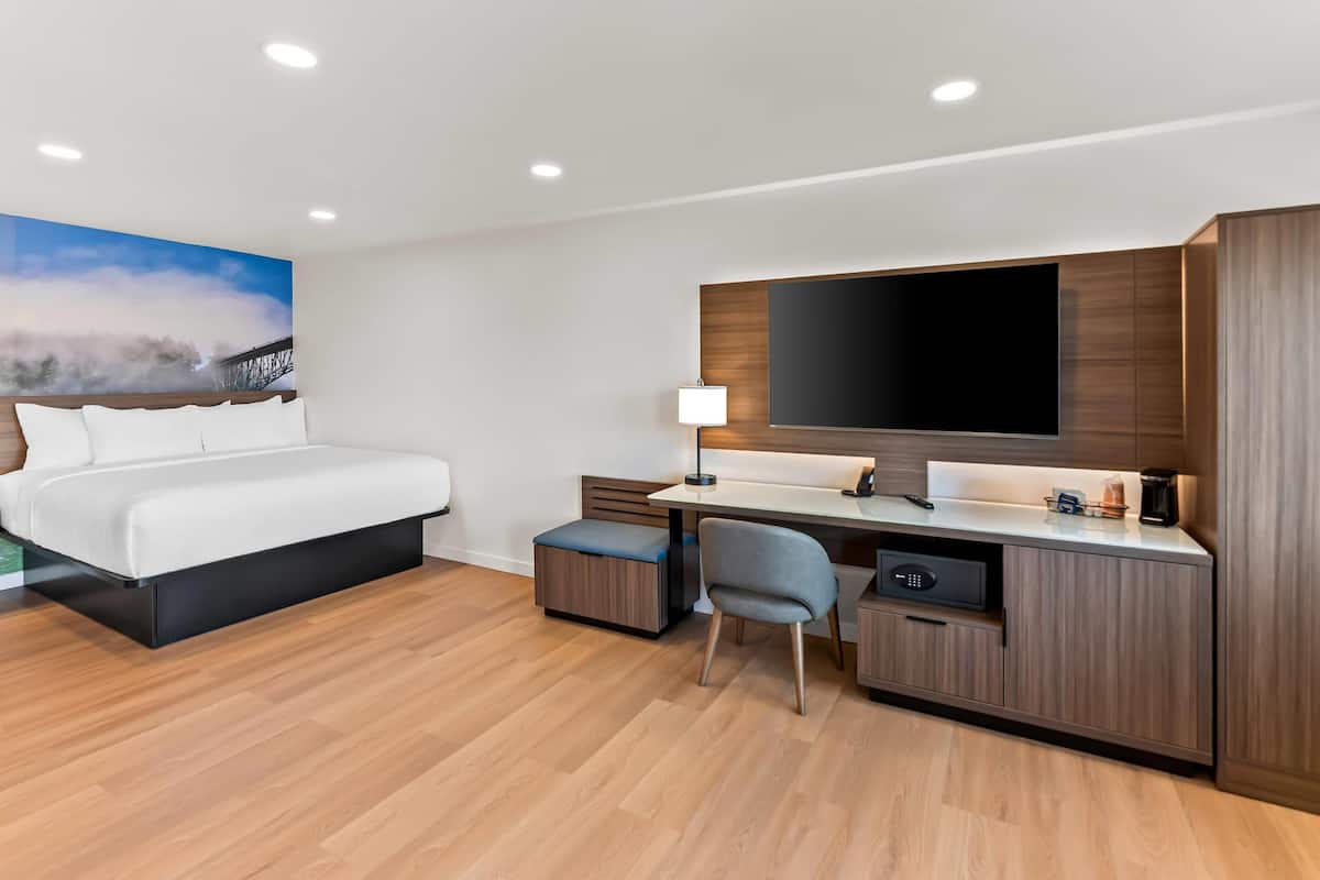 A modern hotel room with a bed, desk, and TV.