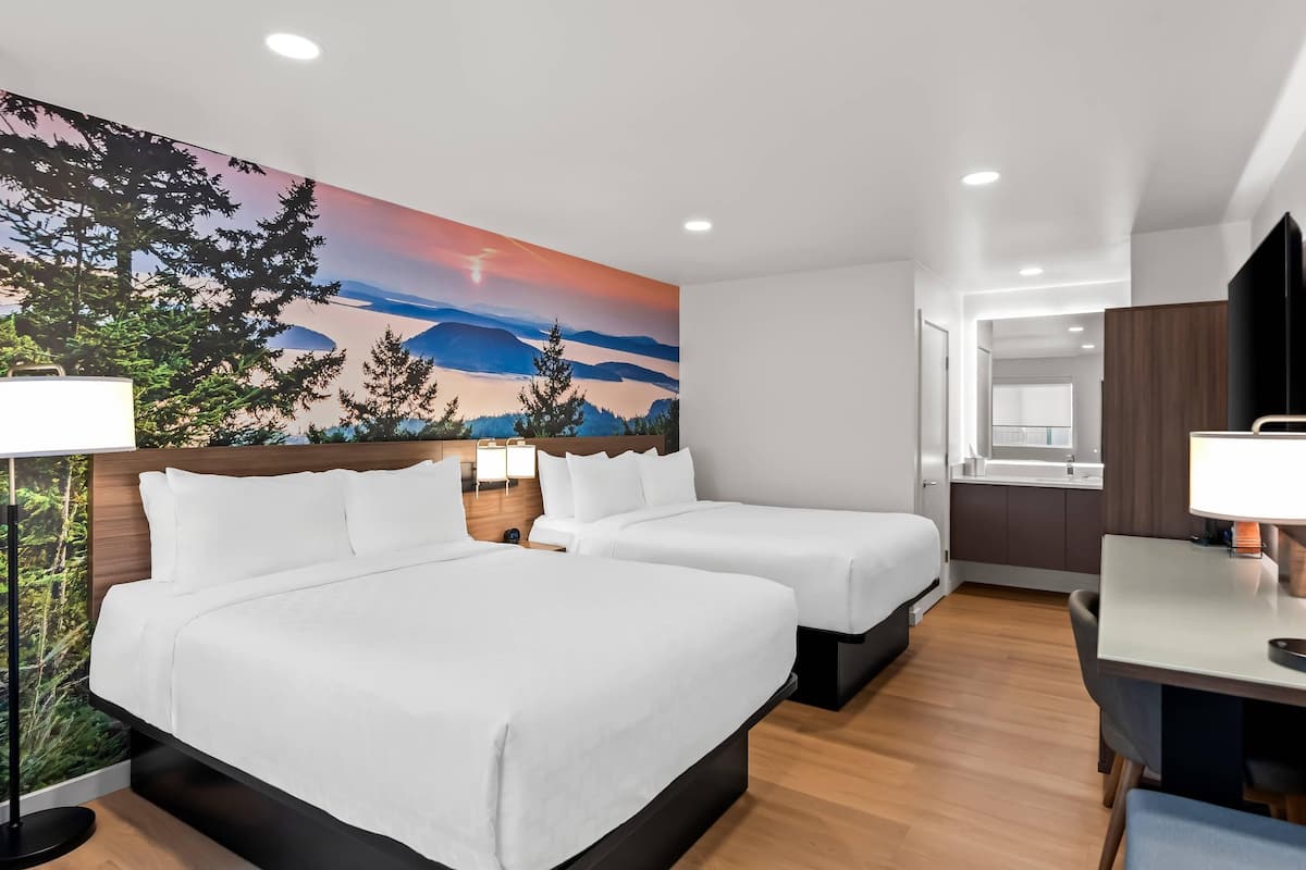 A hotel room with two beds, a desk, and a large wall mural of a landscape.