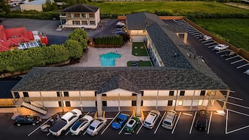 A multi-story hotel with a swimming pool, parking lot, and a covered outdoor area.