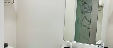 A modern bathroom with a white toilet, a large mirror, and a white sink.