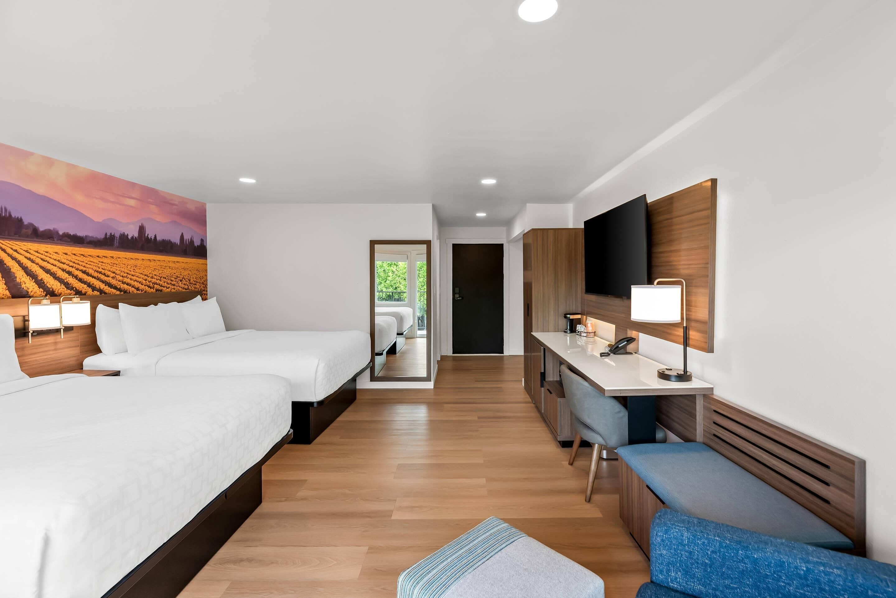 Una habitación de hotel moderna con dos camas, un escritorio, un banco y un televisor grande.