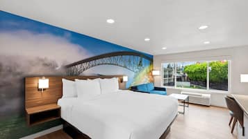 A modern hotel room with a large bed, a nightstand, a desk, and a view of a bridge through a window.