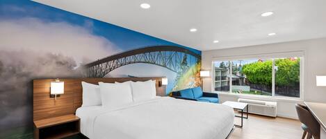 A modern hotel room with a large bed, a nightstand, a desk, and a view of a bridge through a window.