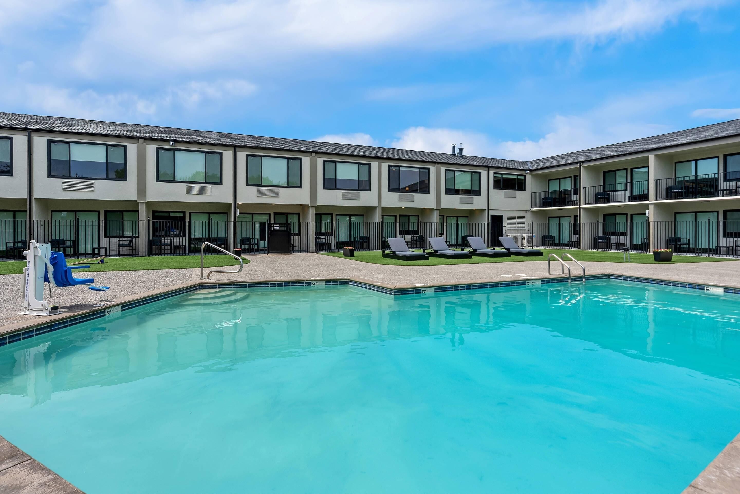 A swimming pool with lounge chairs and a building with multiple balconies.