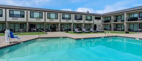 A swimming pool with lounge chairs and a building with multiple balconies.