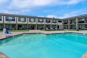 Una piscina con sillones de descanso y un edificio con varios balcones.