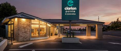 A hotel entrance with a sign for Clarion Pointe by Choice Hotels, featuring a brick facade, large windows, and a covered parking area.