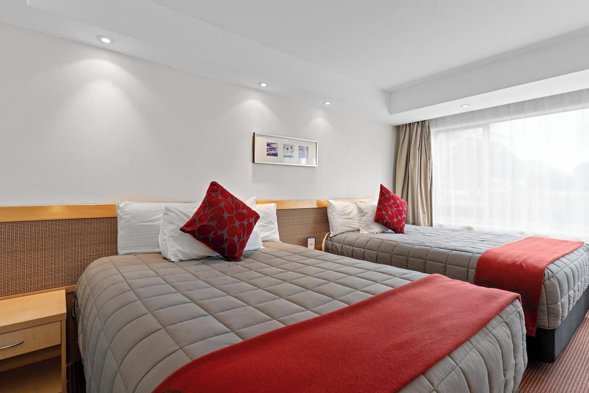 Habitación de hotel con dos camas, cada una con almohada roja, cabecero de madera y un cuadro en la pared.