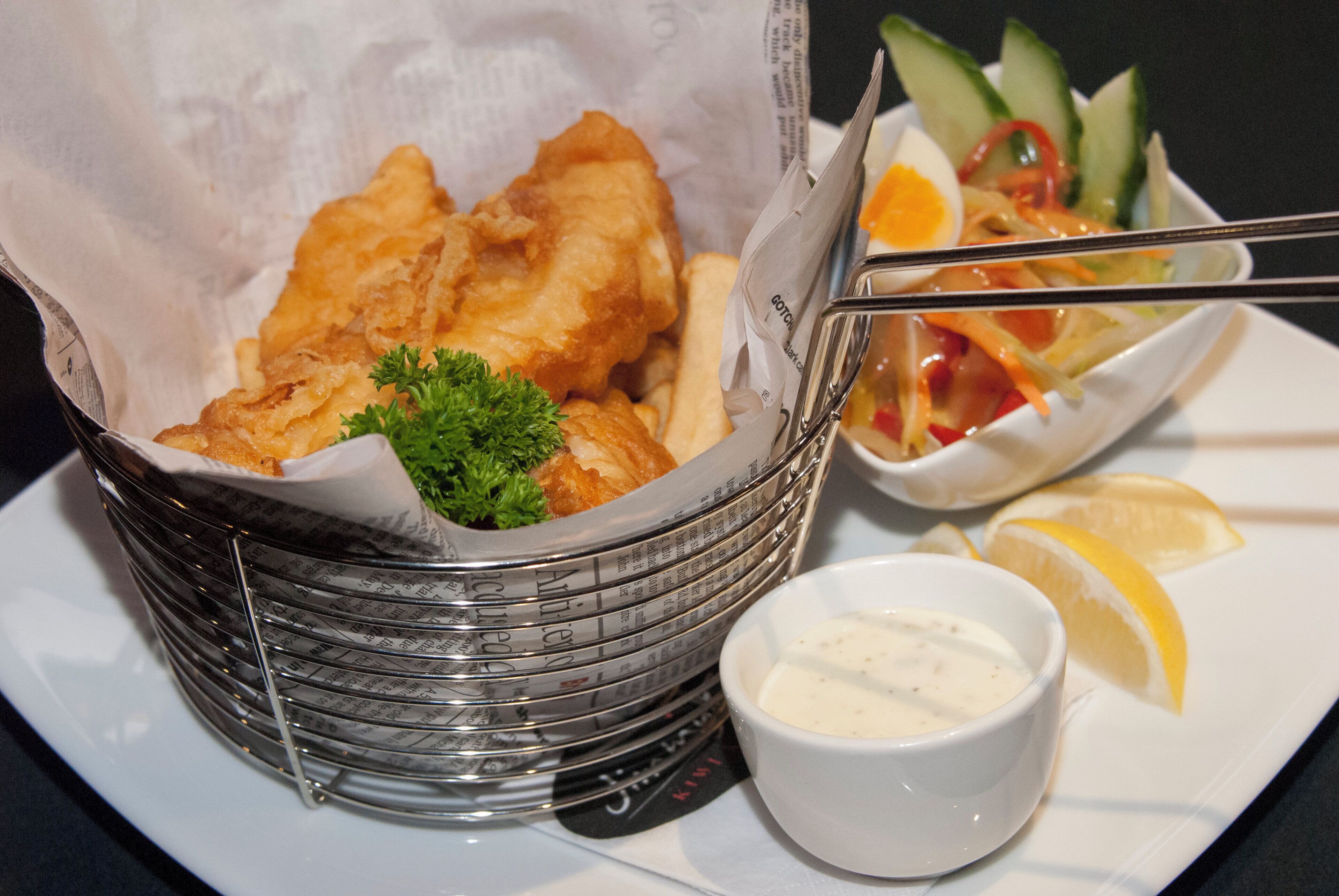 A basket of fish and chips, a salad, and a small bowl of sauce on a plate.