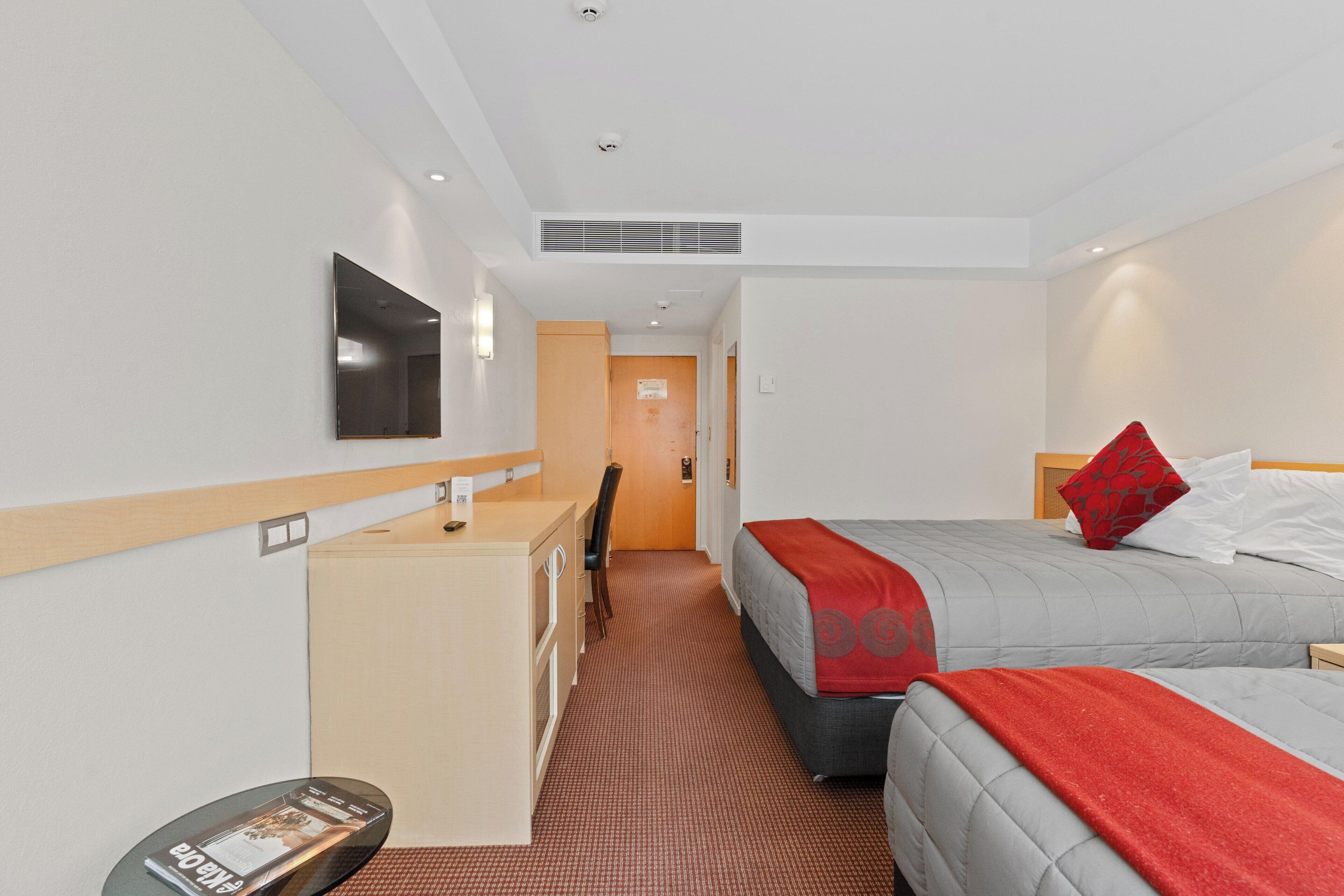 Una camera d'albergo con un letto, una scrivania, una sedia, una televisione e una porta che dà su un'altra stanza.