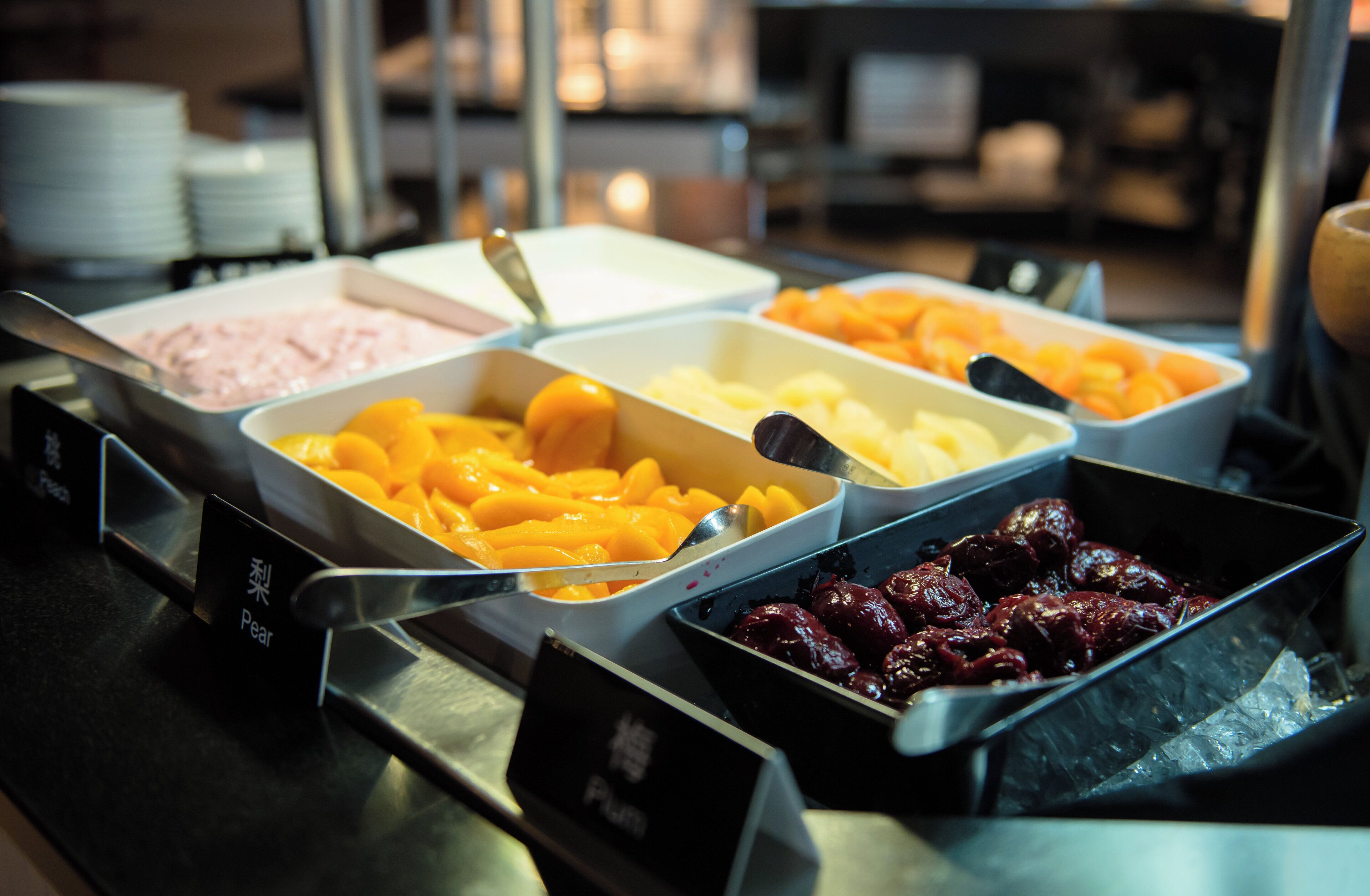 A buffet with labeled food sections including pears, peaches, and plums.