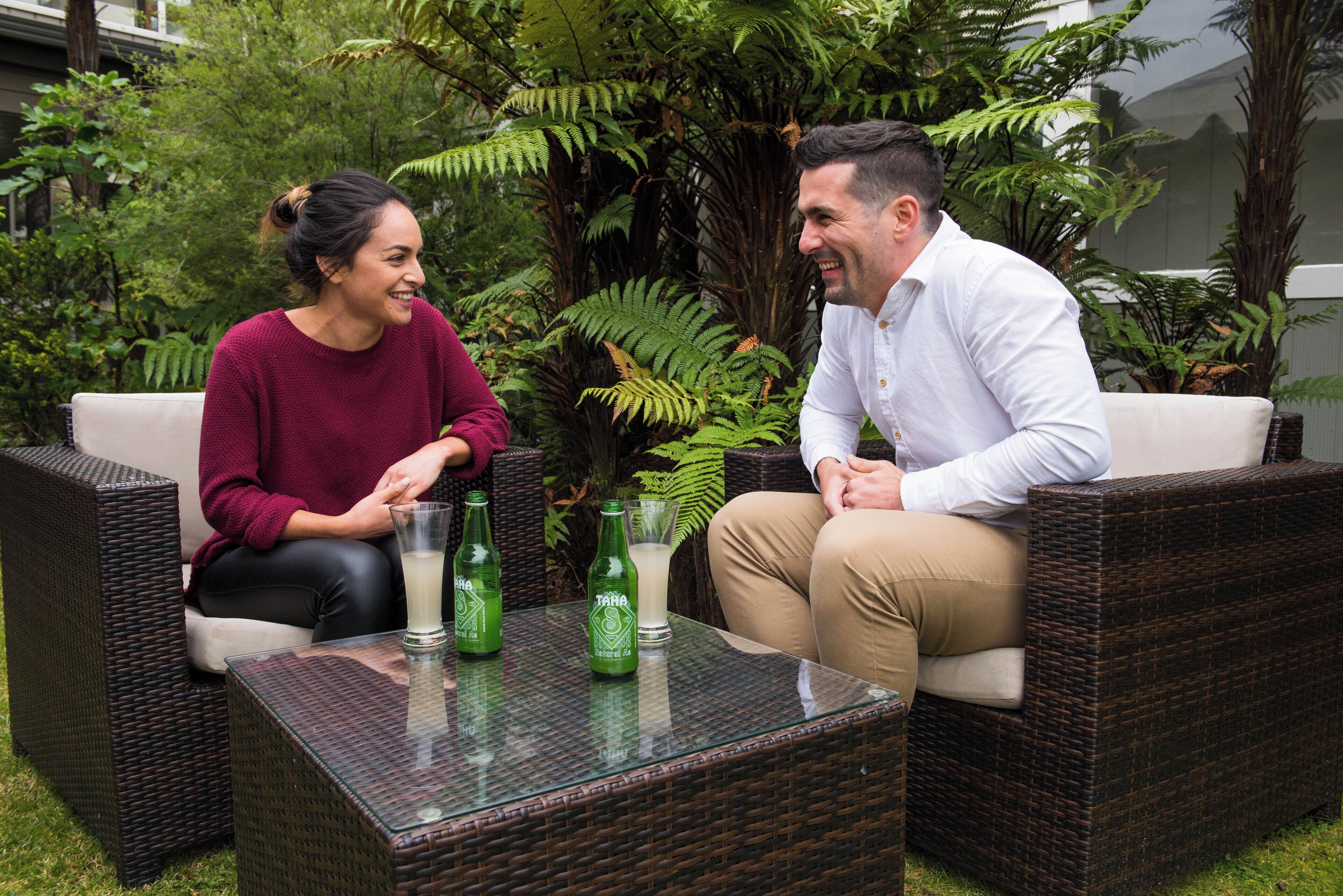Two people seated on wicker sofas with a glass table between them.