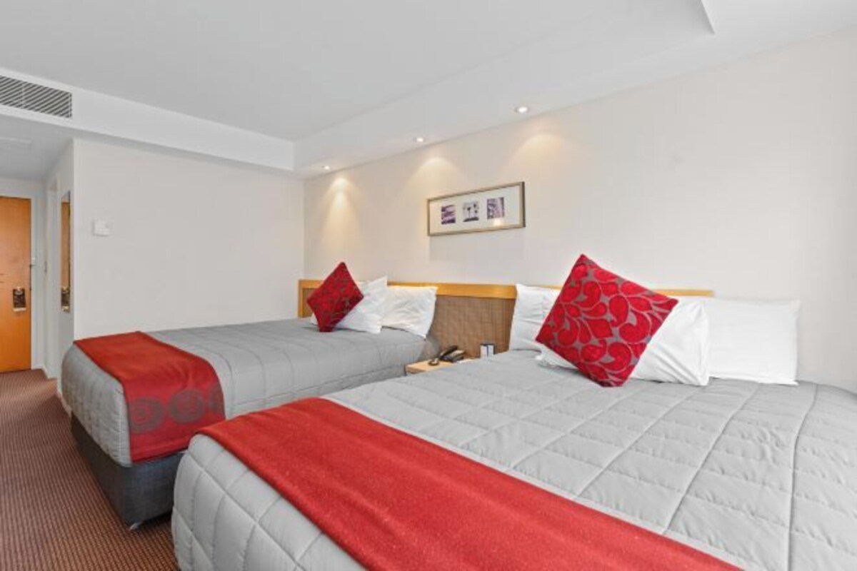 Habitación de hotel con dos camas, cada una con una manta roja y gris, un cabecero de madera y un cuadro en la pared.