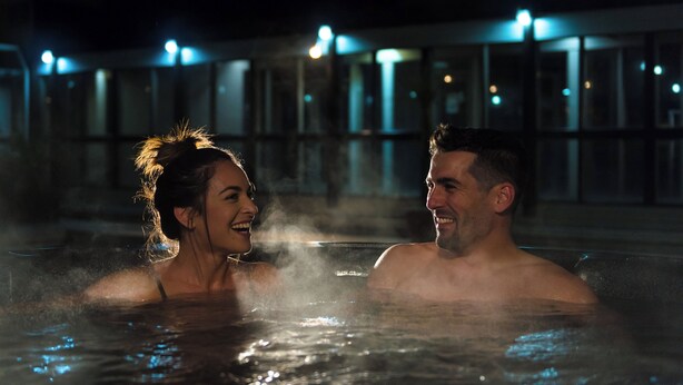 A couple in a hot tub at night with a building in the background. - Copthorne Hotel Rotorua (Rotorua)
