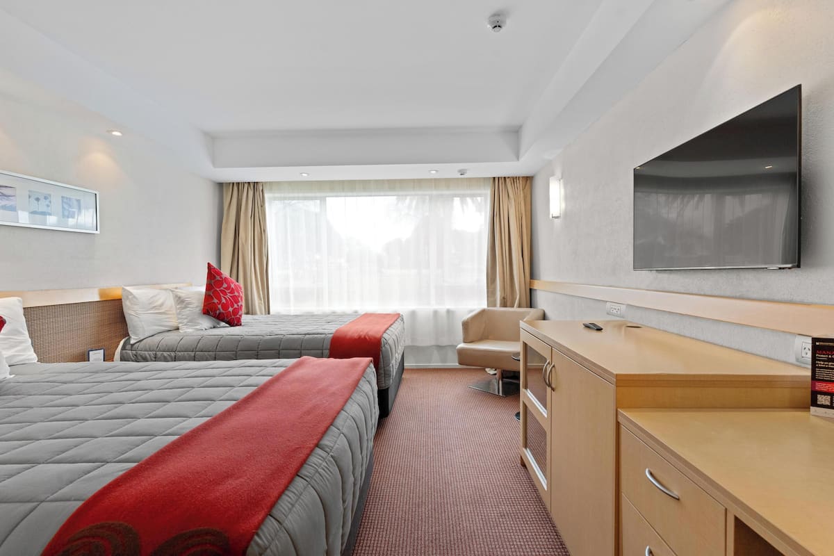 Habitación de hotel con dos camas, un escritorio, un televisor y una ventana con cortinas.