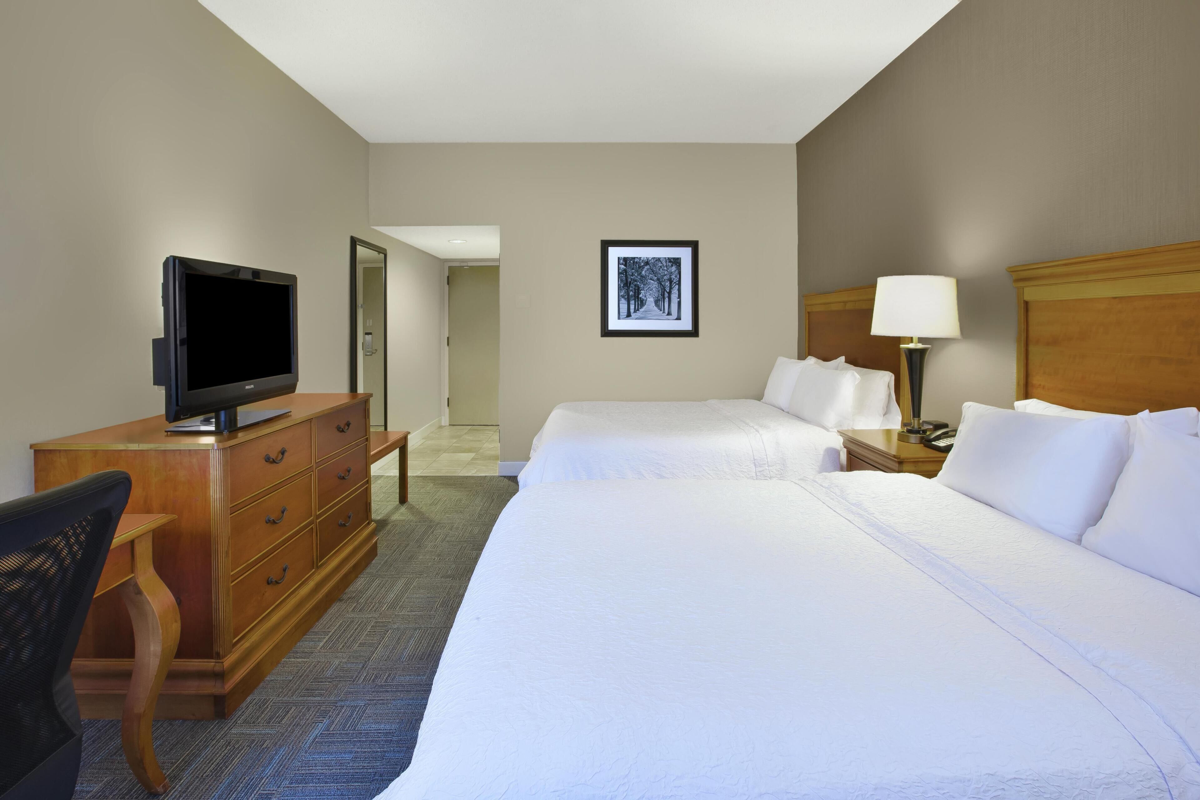 A hotel room with two beds, a television, a desk, and a chair.