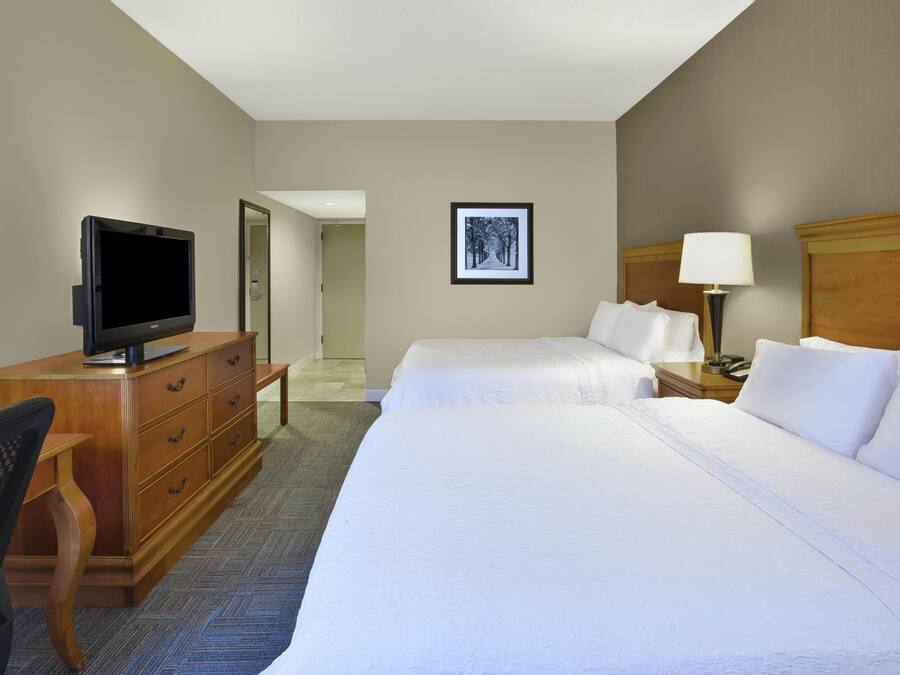 A hotel room with two beds, a television, a desk, and a chair.