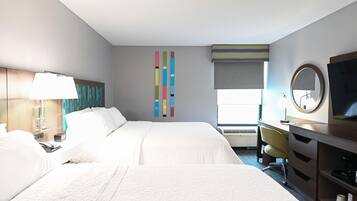 A hotel room with a large bed, a desk with a chair, a TV, a lamp, and a window with blinds.