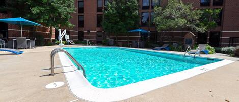 A swimming pool with lounge chairs and umbrellas, surrounded by a brick building.