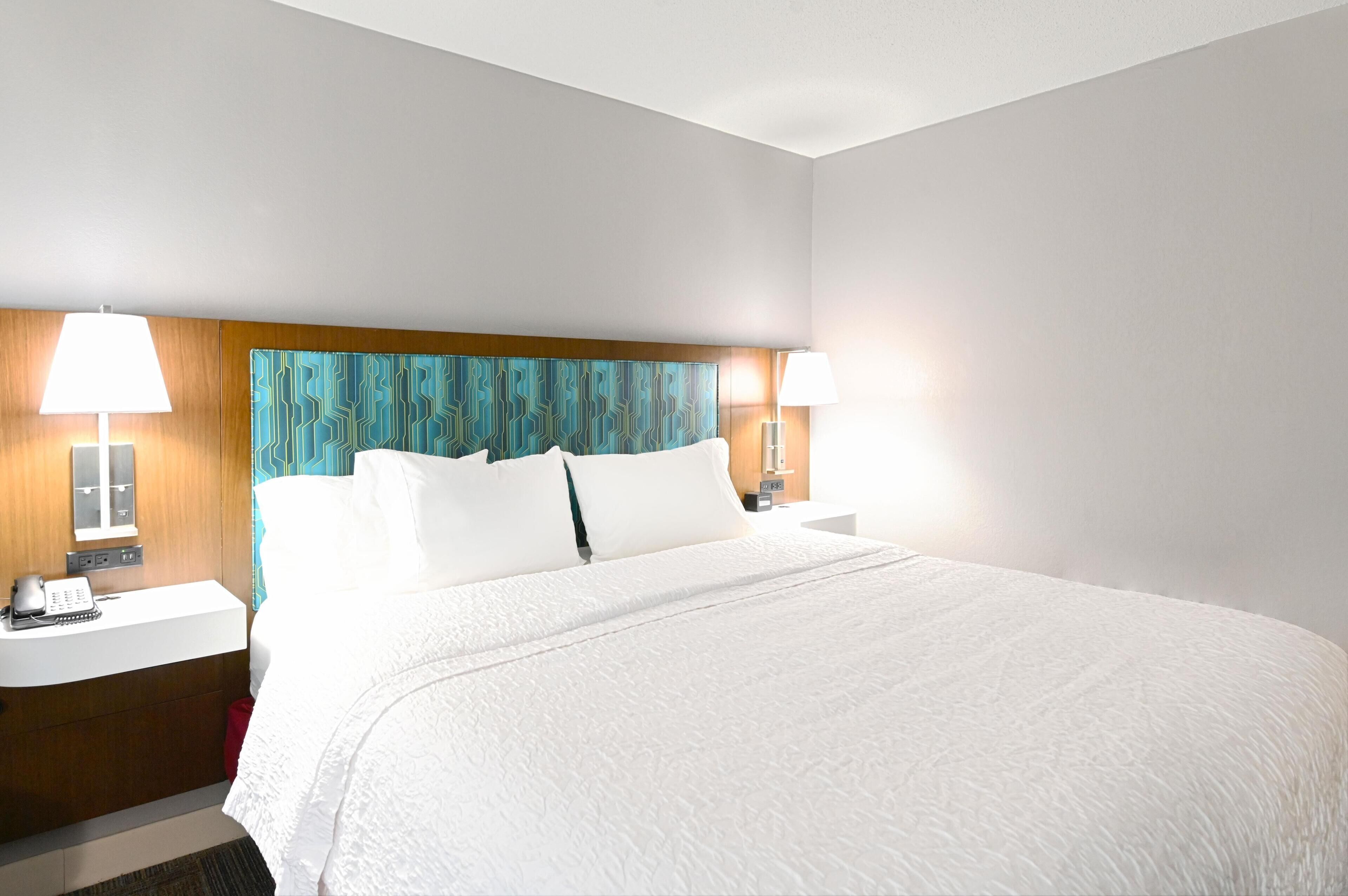 A hotel room with a large bed, two bedside tables, a nightstand, and a headboard with a patterned design.