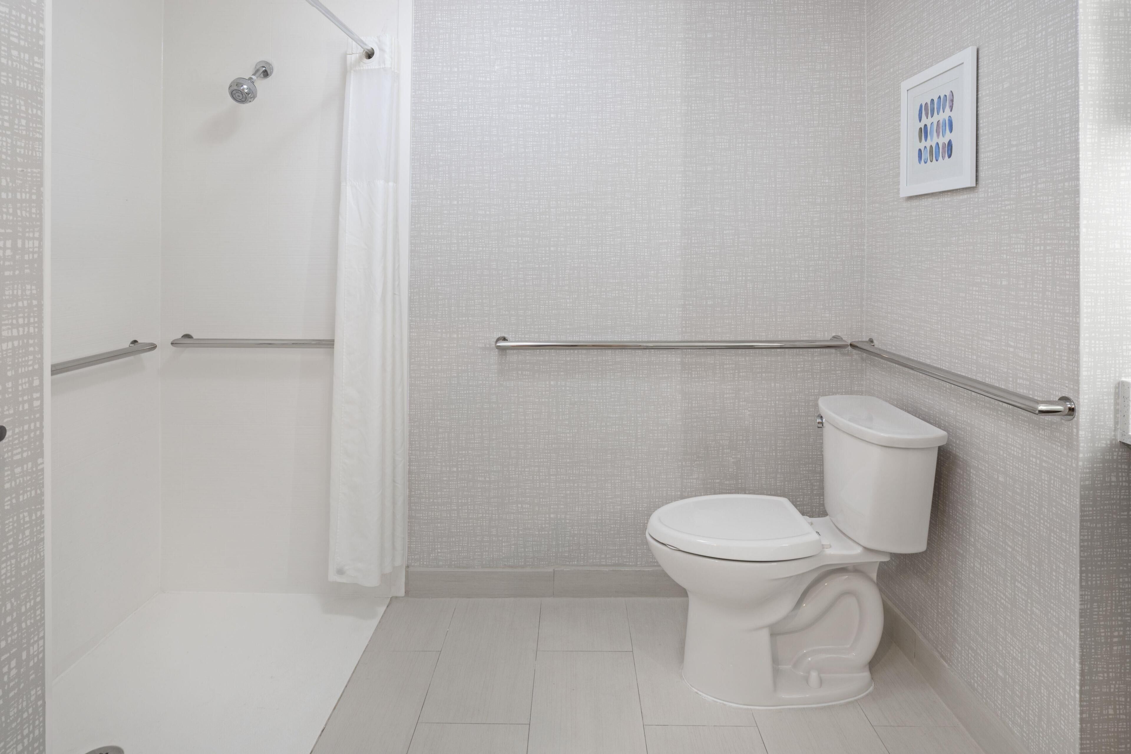 A bathroom with a shower, toilet, and grab bars.