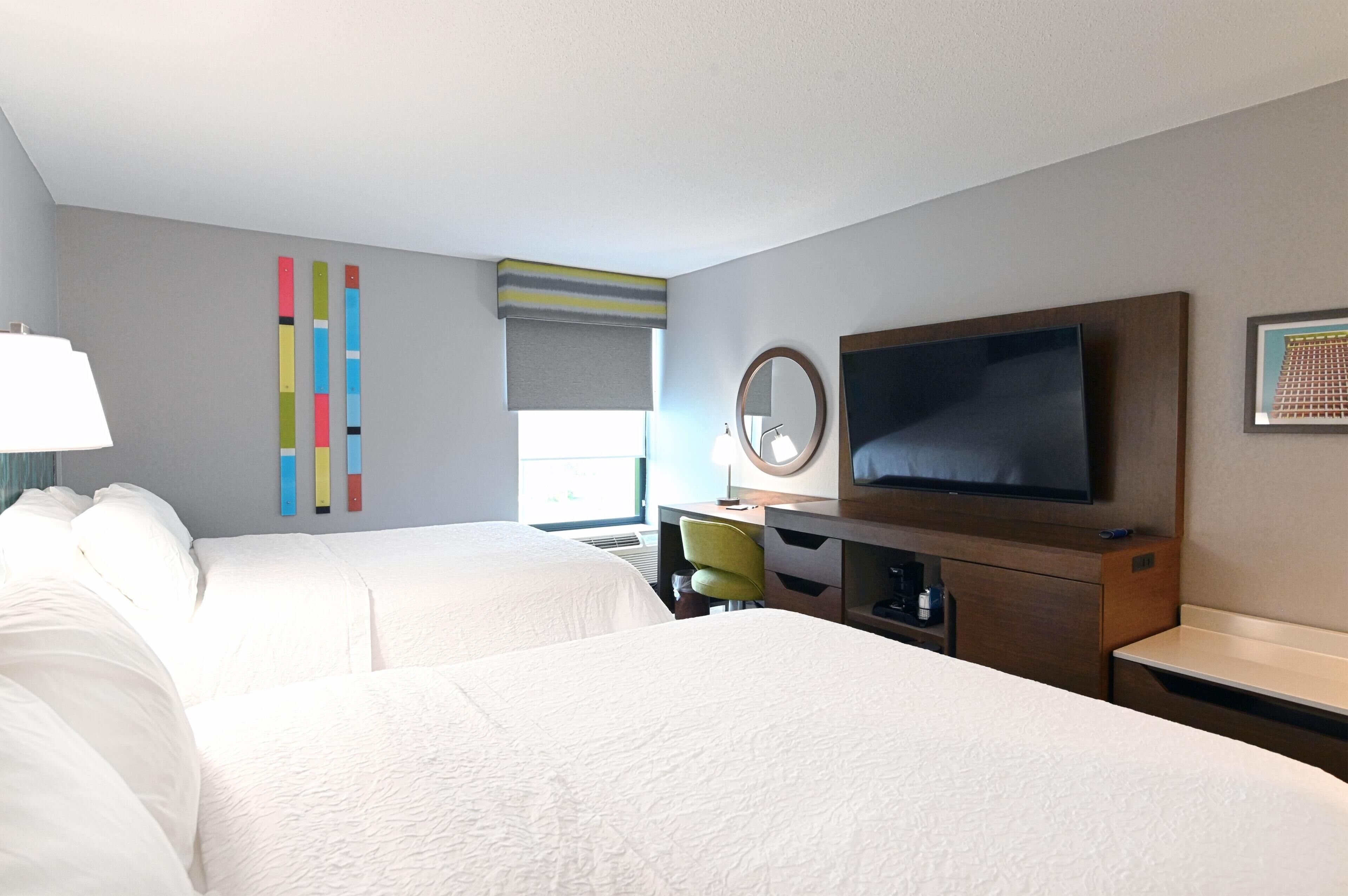 A hotel room with two beds, a desk, a television, and a window with blinds.