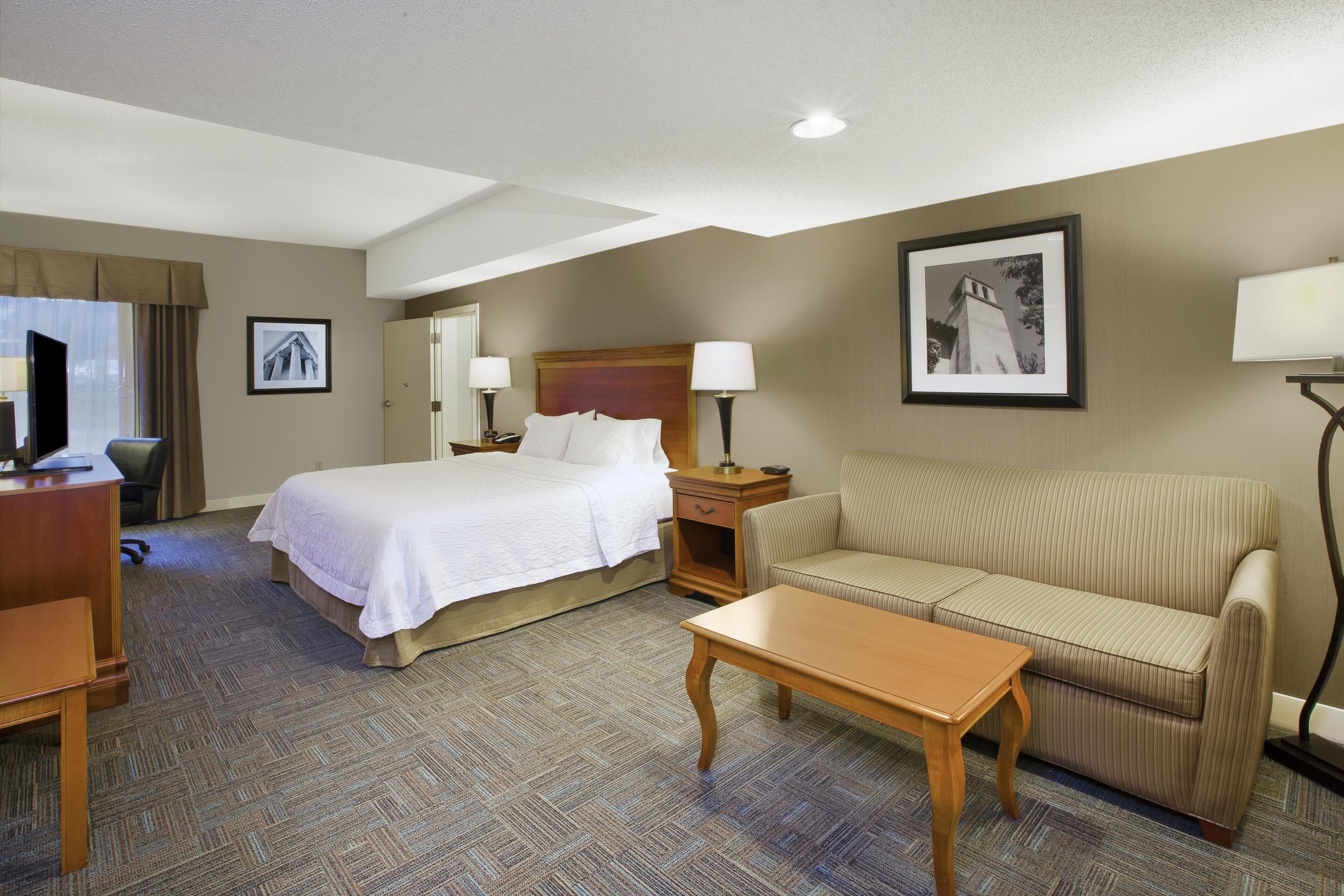 Ein Hotelzimmer mit Bett, Sofa, Schreibtisch, Stuhl und Lampe.