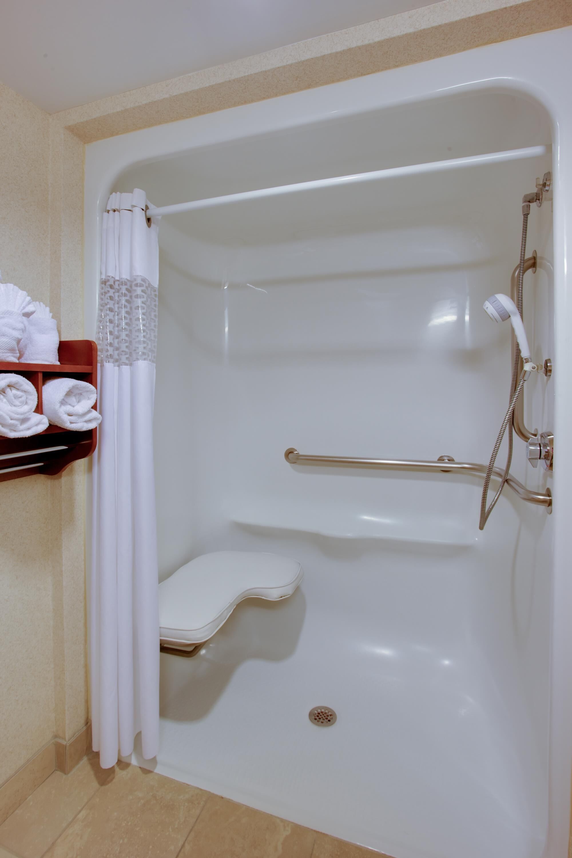 Una bañera con cabezal de ducha, barra de apoyo y repisa con toallas.