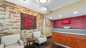 Una zona de recepción con pared de piedra, un letrero de Red Roof Inn, una pantalla de televisión que anuncia Wi-Fi gratuito y un mostrador de recepción.