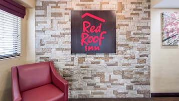 A Red Roof Inn sign on a stone wall, a red leather chair, and a wooden floor.