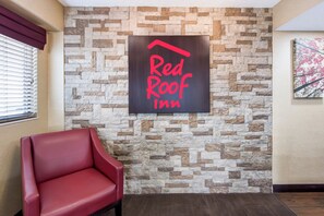 Ein Schild des Red Roof Inn an einer Steinmauer, ein roter Ledersessel und ein Holzboden.