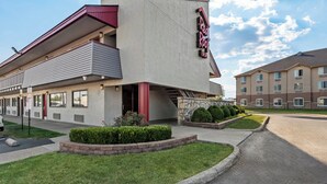 Un motel con diseño moderno, que destaca un letrero rojo y blanco, una zona de estacionamiento techada y un césped bien cuidado.