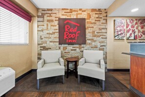 Die Lobby eines Red Roof Inn mit einer Steinsäule, zwei weißen Sesseln, einem kleinen runden Tisch und einer Rezeption.