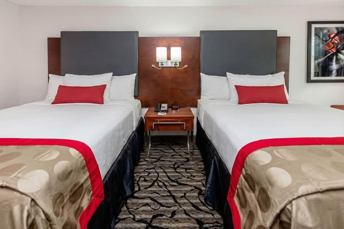A hotel room with two beds, a nightstand, and a telephone.
