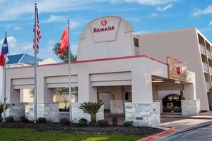 Un hotel Ramada con una fachada moderna, pilares de piedra y varias banderas.
