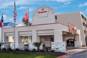 A Ramada hotel with a modern facade, stone pillars, and multiple flags.