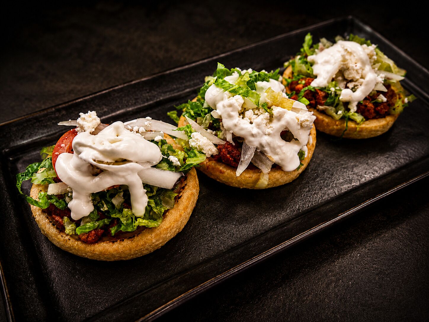 Tres sándwiches abiertos sobre una bandeja negra.